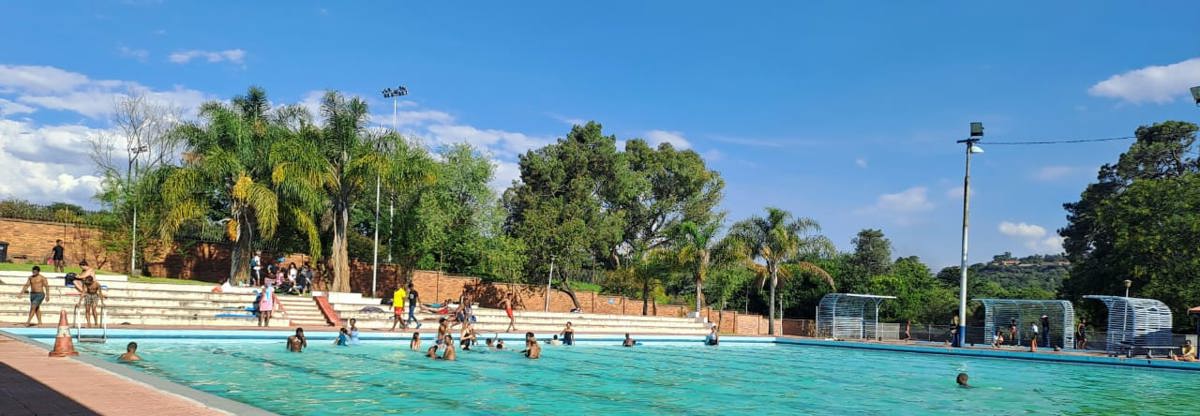ohannesburg residents beside the historic Zoo Lake swimming pool on a bright summer day.