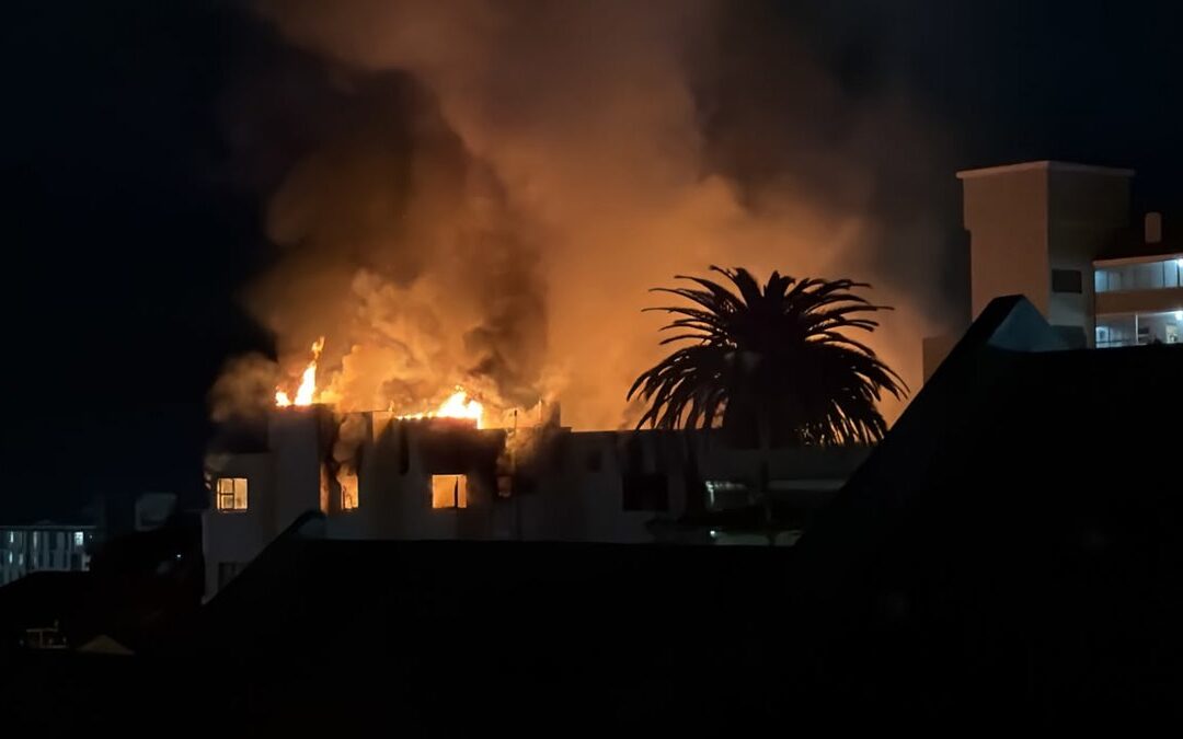 The Dorchester apartment building in Sea Point after the fire, with emergency crews and community members nearby.