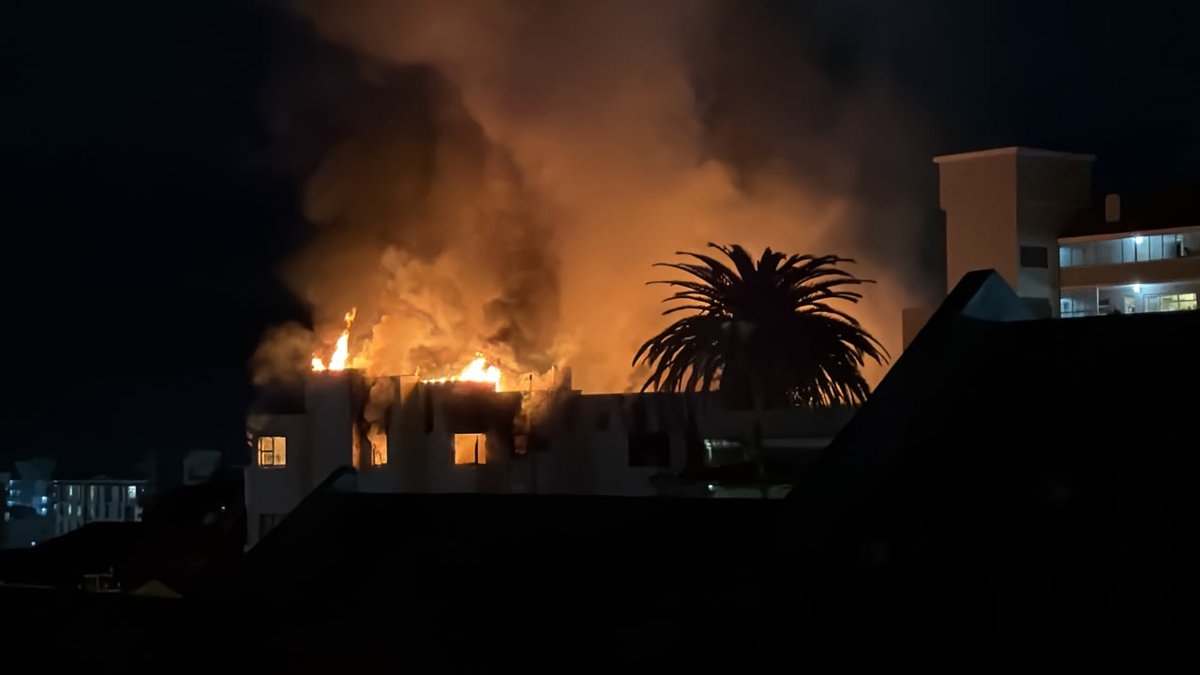 The Dorchester apartment building in Sea Point after the fire, with emergency crews and community members nearby.